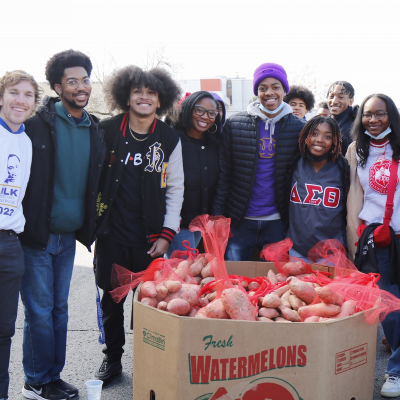 students smiling next to a box full of bagged sweet potatoes