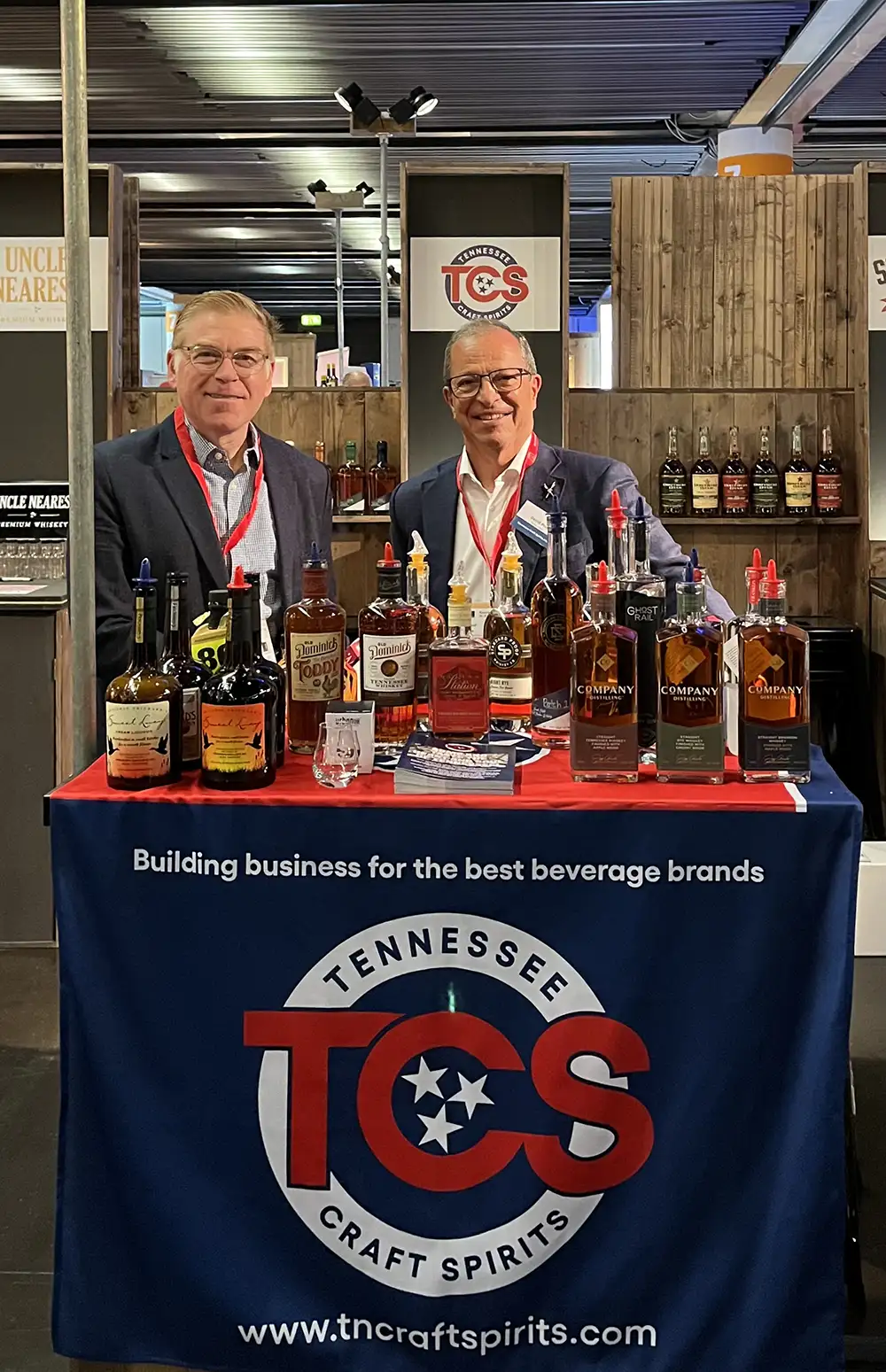 Two men stand behind a Tennessee Craft Spirits booth displaying bottles of whiskey and craft spirits at a trade show.