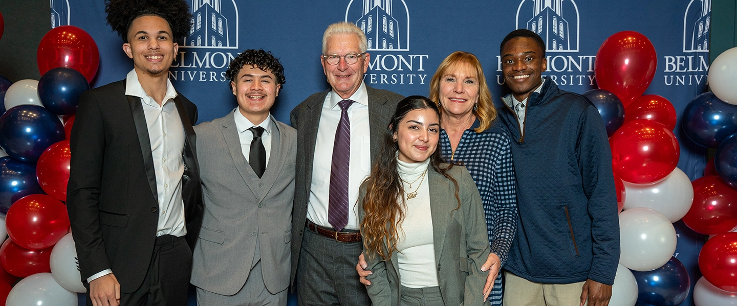 Group of six people posing in front of a Belmont University backdrop with red, white and blue balloons, smiling at a campus celebration or donor event.