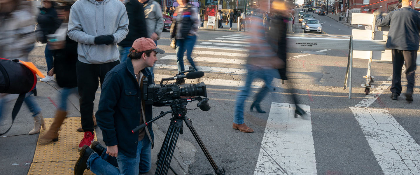 Two students filming on a busy street in Nashville with people walking by
