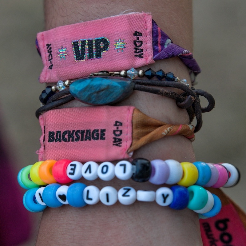 A close up photo of a person's wrist with their festival passes and beaded bracelets