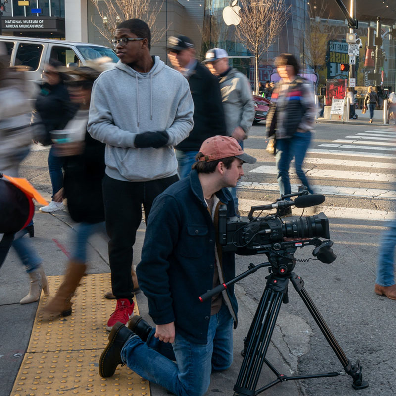 Two students filming on a busy street in Nashville with people walking by