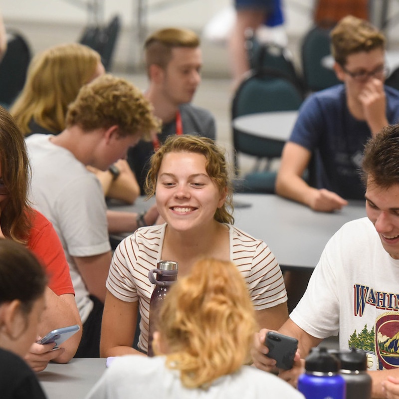 Student smiles at a table with other students