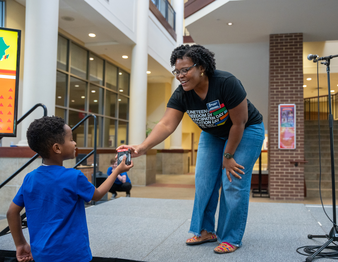 Woman in black Juneteenth shirt hand game to young boy in blue shirt