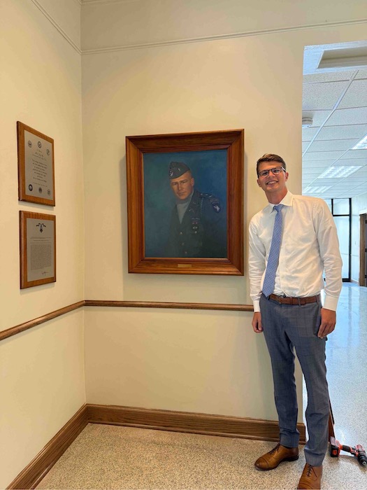 Harry Crane poses next to portrait of Jimmy Gardner in courthouse. 