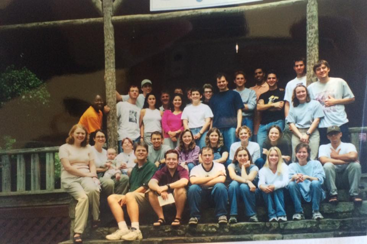 Diverse group of young adults smiling outdoors by the ocean, friends on a coastal trip.