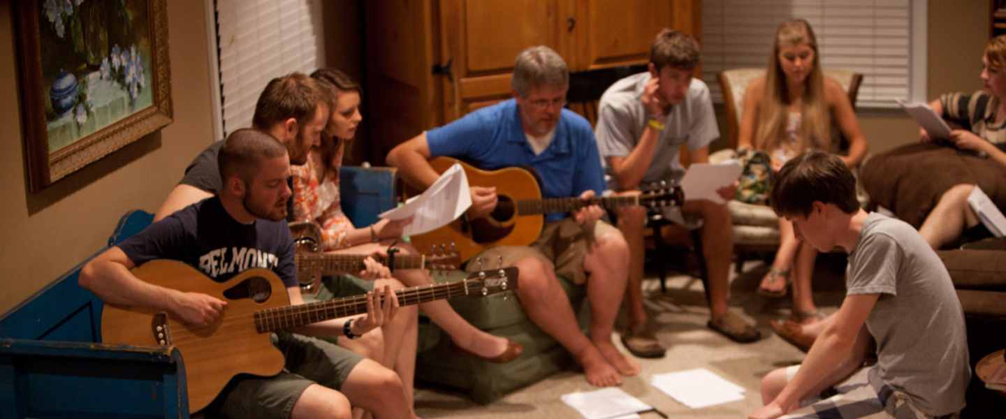 Group of people playing acoustic guitars and reading sheet music during an informal music session indoors.