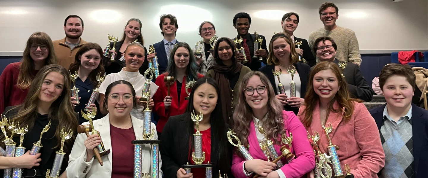 Speech and Debate students proudly holding many trophies and awards, celebrating a competition victory.