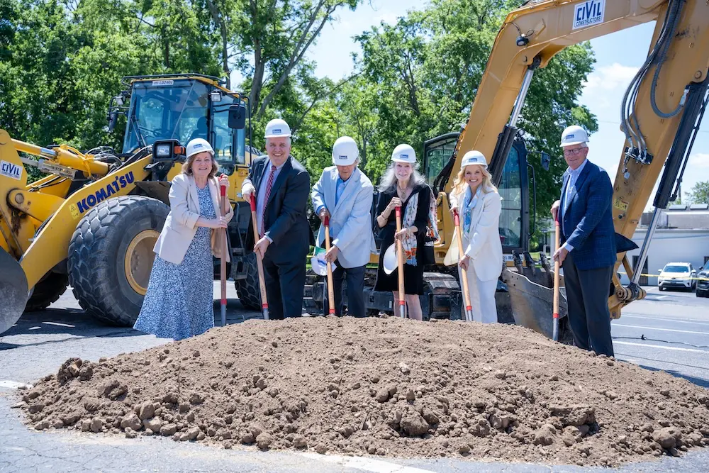 Six people with construction helmets shovel mound of dirt