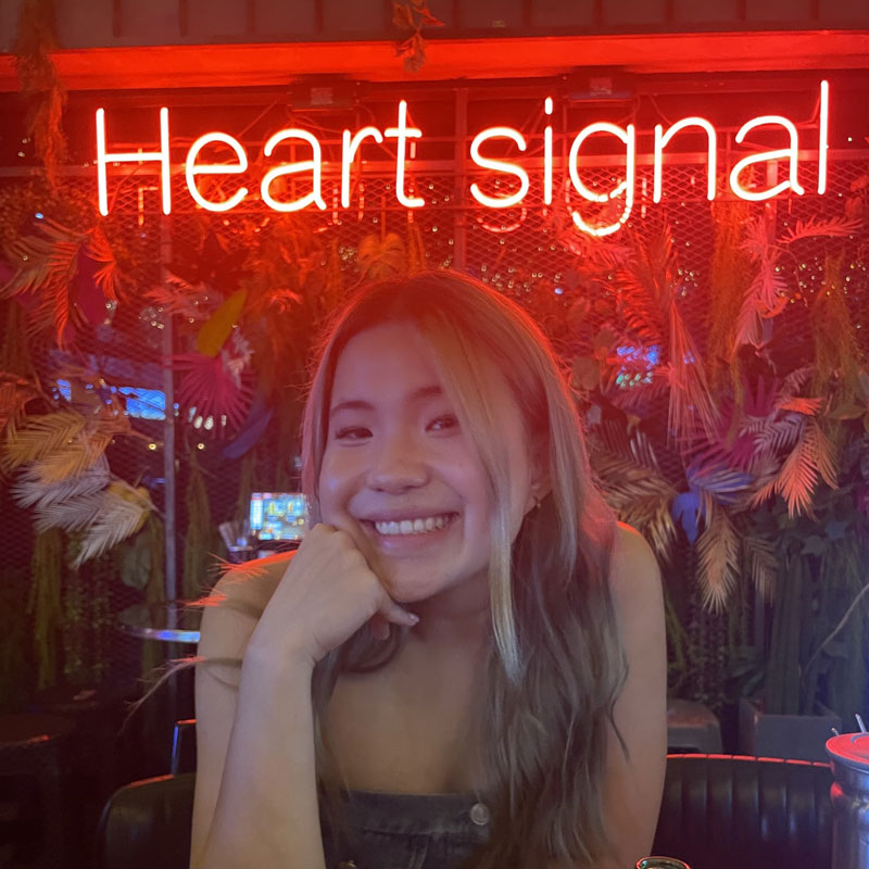 Student smiling in front of neon sign