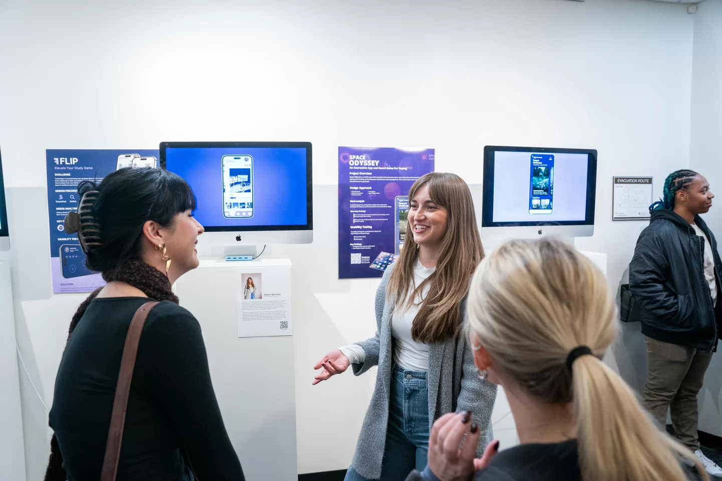 A group of people engage in conversation at Watkins Senior Art Crawl with digital displays on the wall.