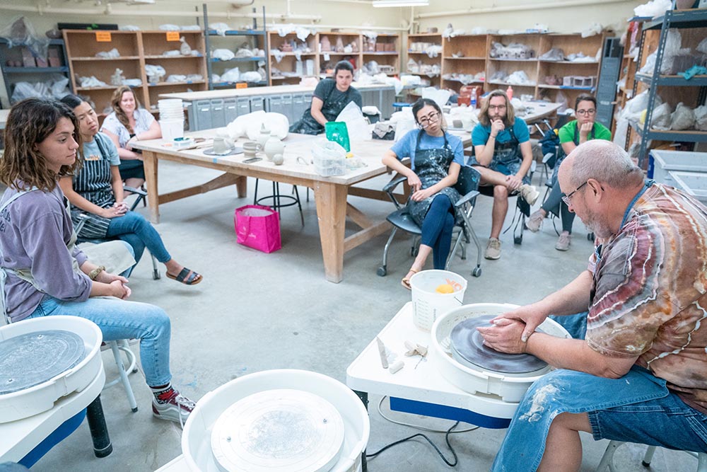 Students watching professor teach pottery class