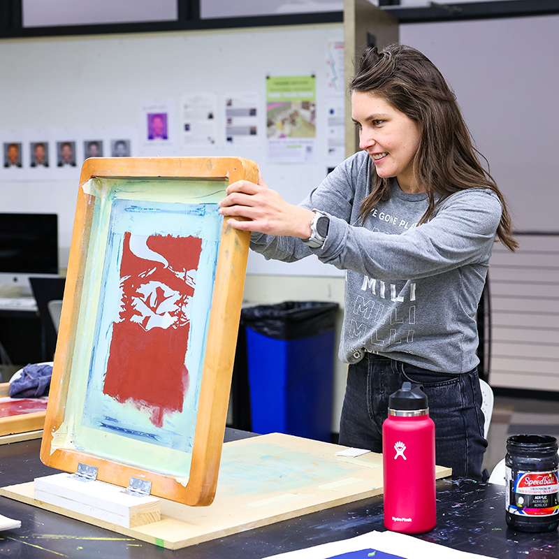 woman with long brown hair tilting up her printing screen to view her poster.