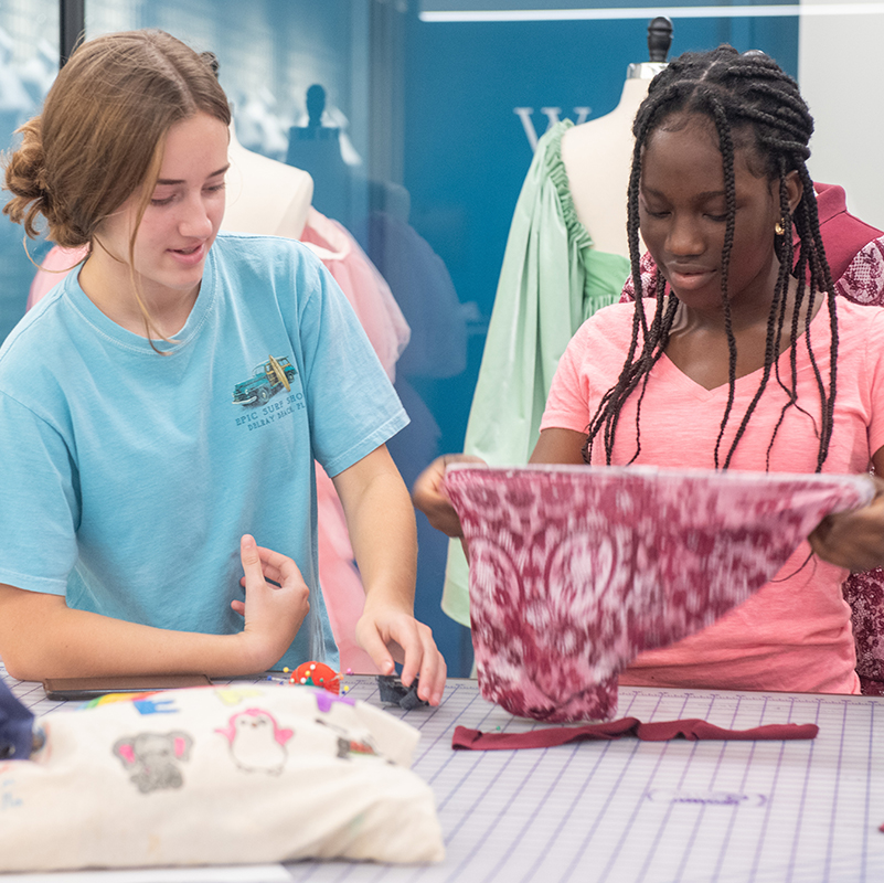 One student holding up a piece of cloth while another student looks on 